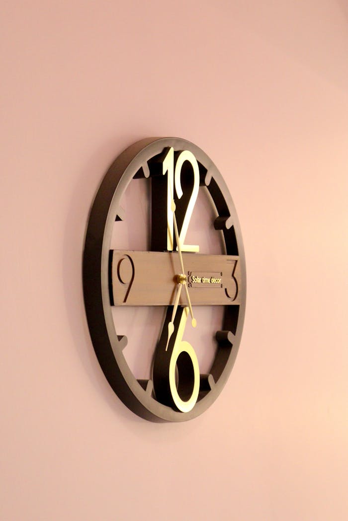Stylish round wall clock with gold accents against a pastel pink background.